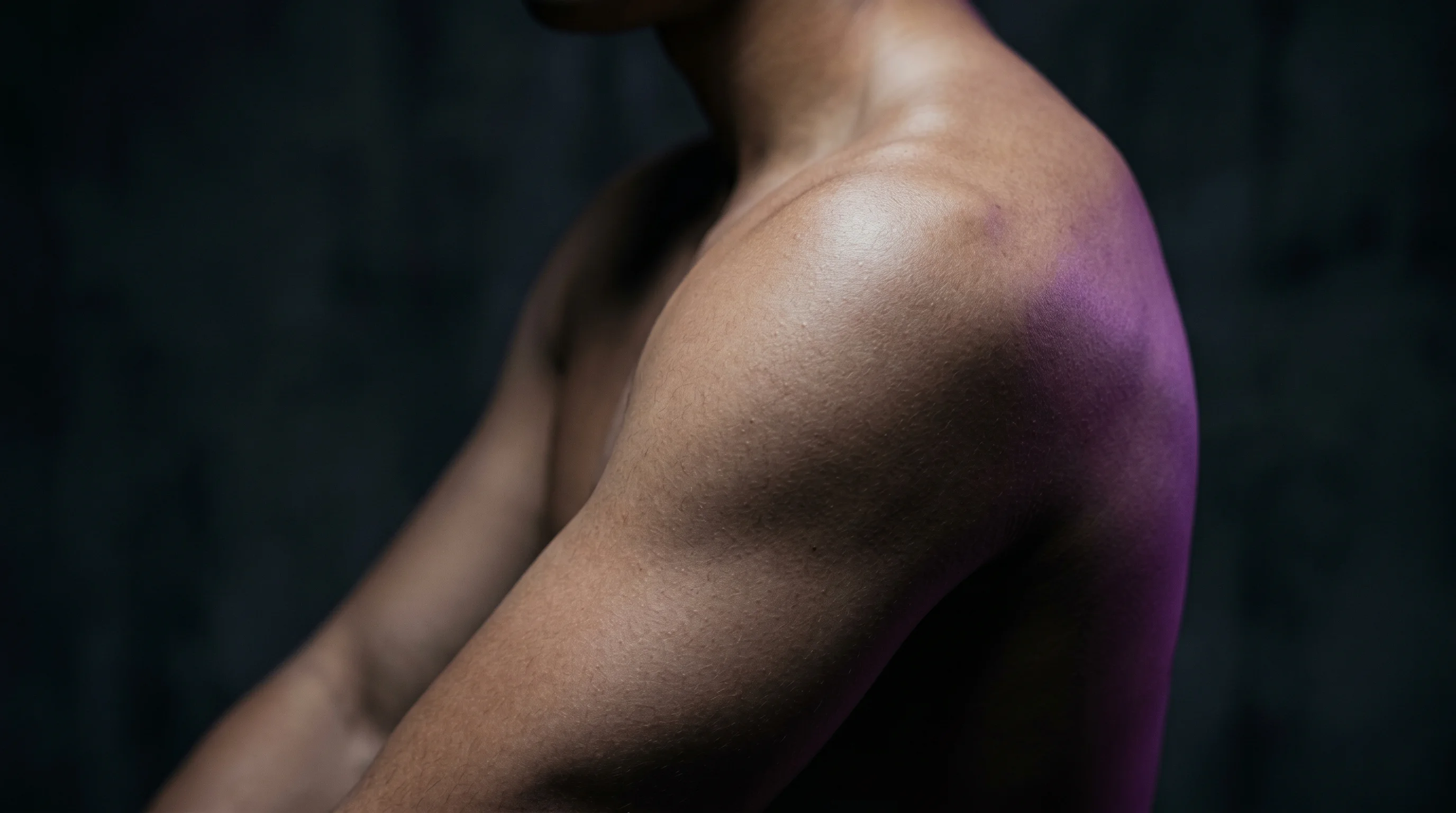 Outer upper arm with clean skin texture, dramatic side rim lighting, dark background, no tattoo visible, editorial photography style