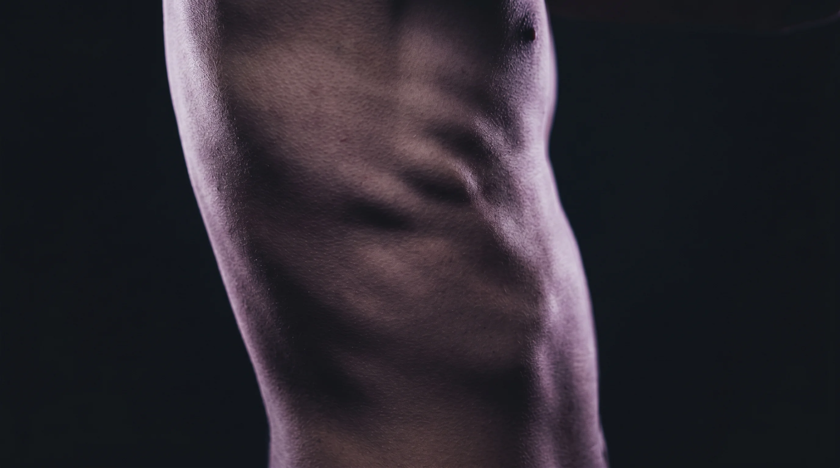 Close-up macro of tattoo needle detail on skin, dramatic directional lighting, very dark background, sharp ink line detail visible, editorial photography