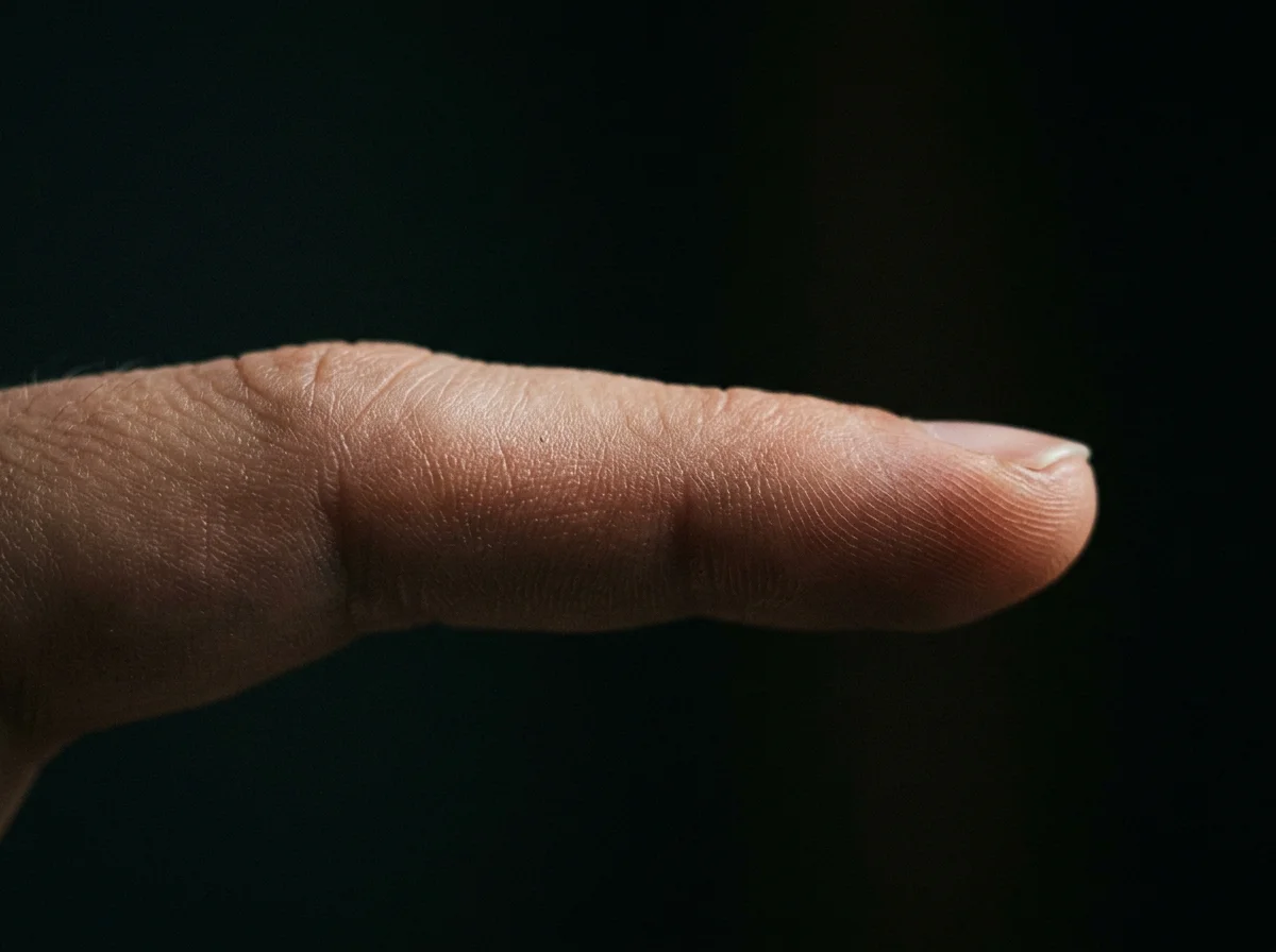A single finger with clean smooth skin, very close macro shot, dramatic dark background, side lighting, no visible tattoo, intimate editorial style photography