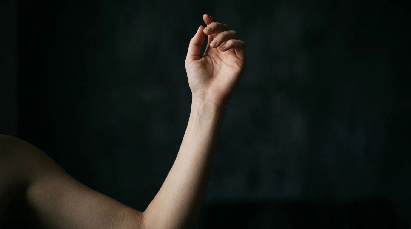 Person examining their forearm in a dark room, holding up their arm to the light, dramatic side lighting from a single source, dark background, introspective mood, editorial photography style, skin texture visible